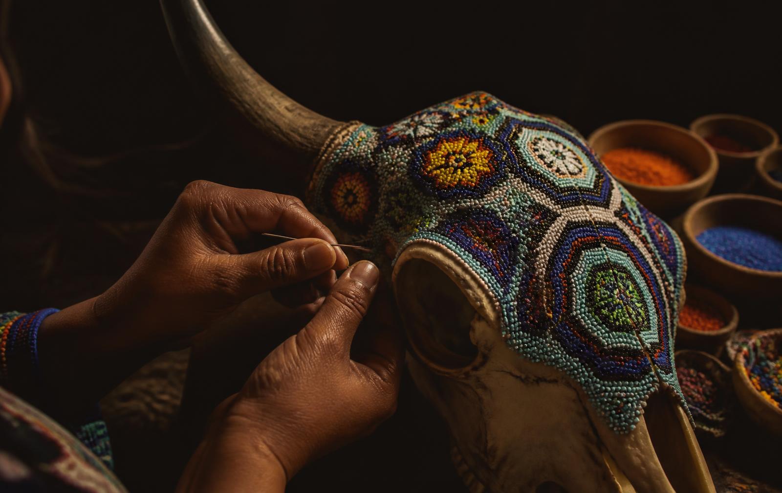 Artesano wixárika colocando chaquira grano por grano sobre un cráneo de toro cubierto de cera de Campeche.