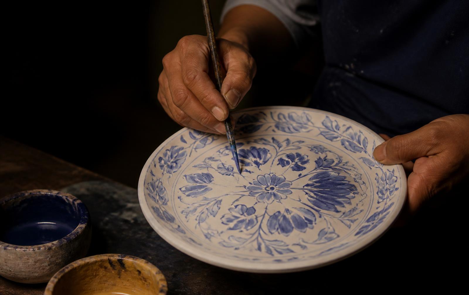 Ceramista poblano pintando a mano libre un plato de talavera con pigmento de cobalto.